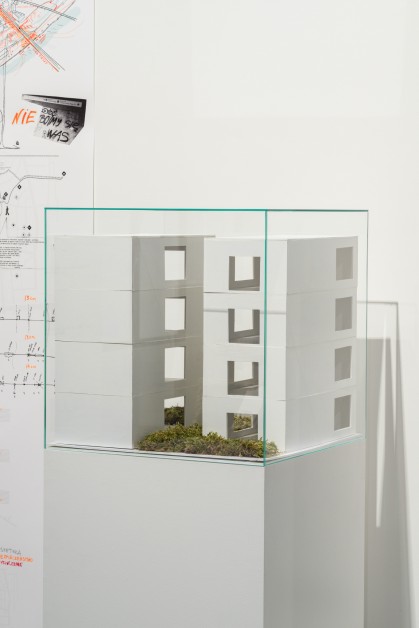 Na postumencie za szkłem znajduje się piankowy model apartamentowców, który ukazuje nano - lofty. Fragmenty zieleni reprezentuje tu mech.     