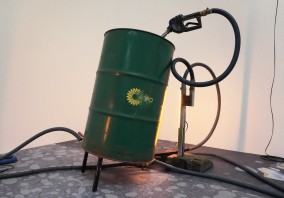 Zielona beczka BP stoi w rogu sali z podłączonym do niej czarnym odkurzaczem. 